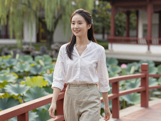 Chinese woman walking through a traditional Chinese garden with red bridge and lotus pond